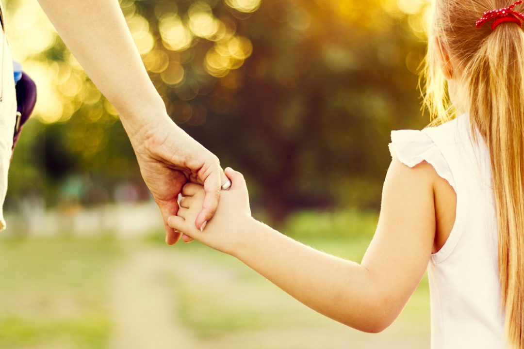 Child holding parents hand on a walk